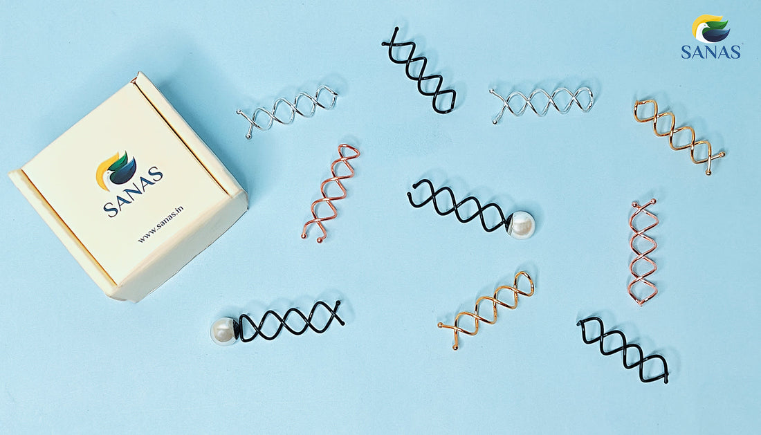 A curated flat lay image showcasing assorted spiral hair pins in black, gold, rose gold, and silver finishes—including single pearl-accented spin pins—on a soft blue background with SANAS branded packaging.