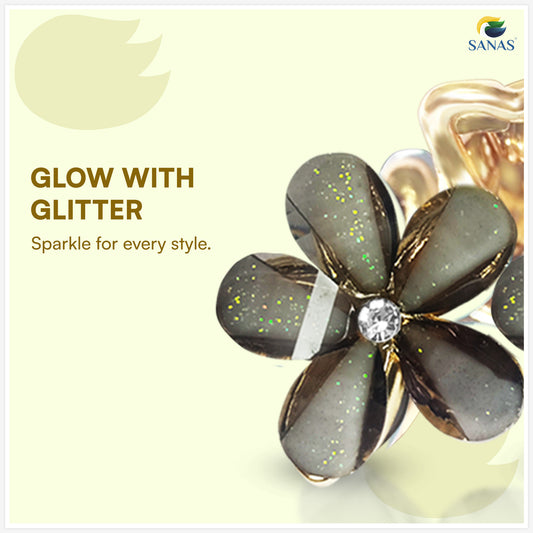 Flower-shaped jewelry with glitter and a diamond, branded 'Sanas', on a light yellow background.
